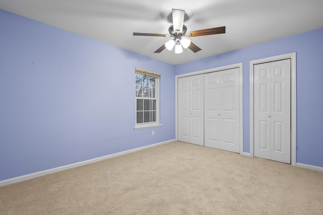 unfurnished bedroom with ceiling fan, light colored carpet, and multiple closets