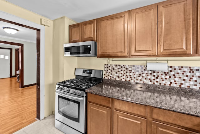 kitchen featuring appliances with stainless steel finishes, dark stone countertops, backsplash, light tile patterned floors, and crown molding