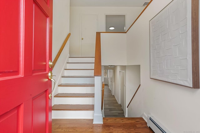 stairs featuring a baseboard heating unit, visible vents, and wood finished floors