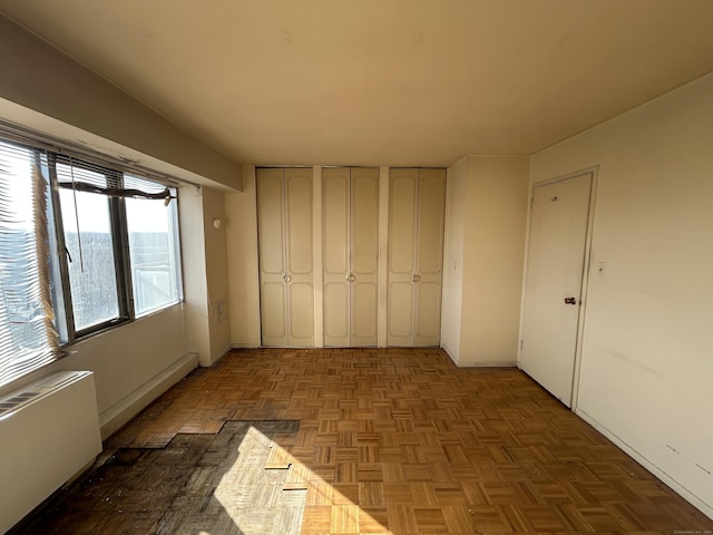 unfurnished bedroom with radiator heating unit, parquet flooring, and multiple closets