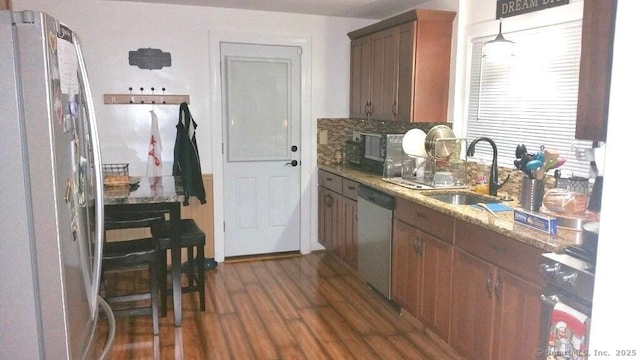 kitchen with appliances with stainless steel finishes, sink, backsplash, light stone counters, and dark wood-type flooring