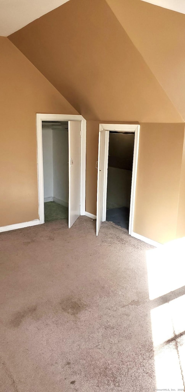 unfurnished bedroom with multiple closets, lofted ceiling, and carpet flooring