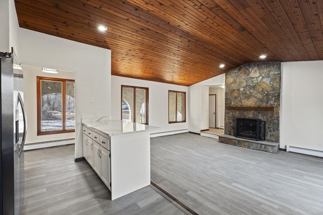 kitchen with light stone counters, stainless steel fridge, white cabinets, a fireplace, and a baseboard heating unit