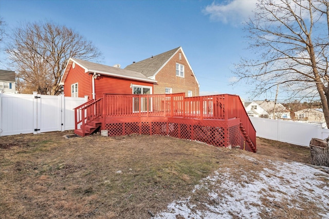 snow covered back of property featuring a wooden deck and a lawn