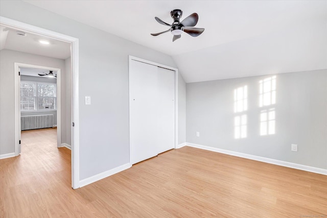 unfurnished bedroom featuring radiator, light hardwood / wood-style flooring, ceiling fan, vaulted ceiling, and a closet