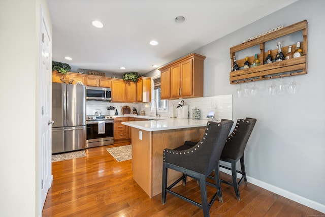 kitchen featuring appliances with stainless steel finishes, tasteful backsplash, a breakfast bar area, kitchen peninsula, and light wood-type flooring