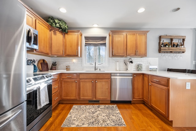 kitchen with sink, decorative backsplash, light hardwood / wood-style flooring, and stainless steel appliances