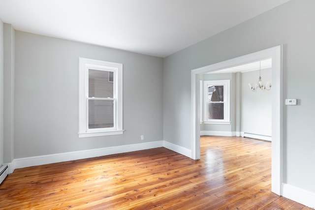 empty room featuring hardwood / wood-style flooring, baseboard heating, and a notable chandelier