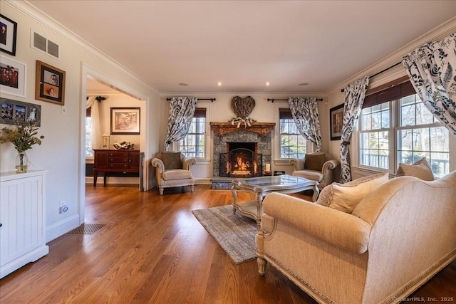 living room featuring wood-type flooring, a stone fireplace, and crown molding