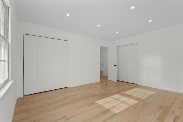 unfurnished bedroom featuring multiple closets and light hardwood / wood-style flooring