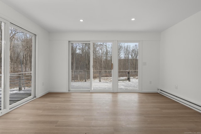 spare room featuring a baseboard heating unit, a healthy amount of sunlight, and light hardwood / wood-style floors