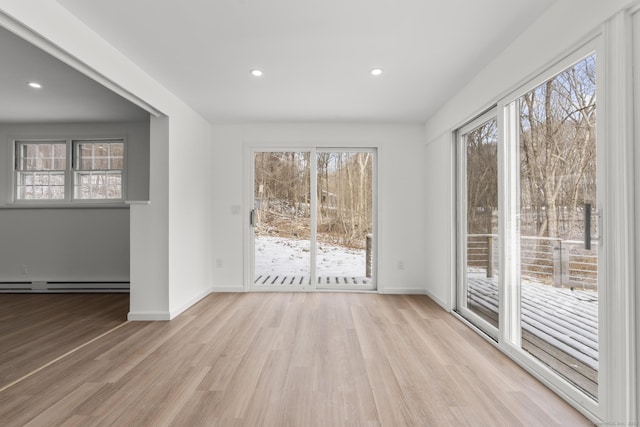 empty room featuring a baseboard heating unit, a wealth of natural light, and light hardwood / wood-style floors