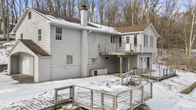 snow covered back of property with a garage, a wooden deck, and a balcony