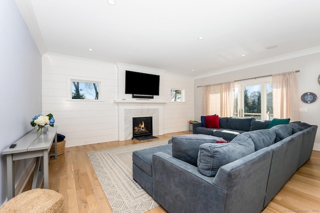 living room with crown molding, a premium fireplace, and light wood-type flooring