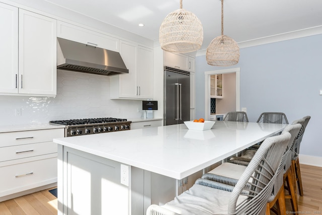 kitchen featuring a kitchen island, wall chimney range hood, a breakfast bar area, and appliances with stainless steel finishes