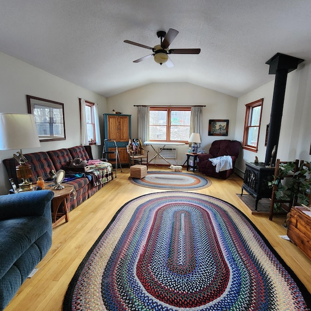 living room featuring a textured ceiling, light hardwood / wood-style flooring, vaulted ceiling, and a wood stove