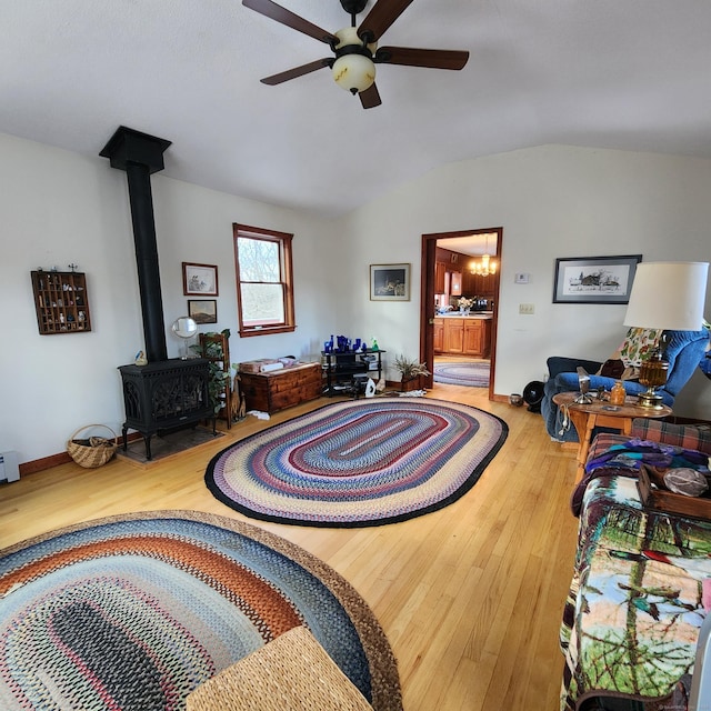 living room with wood-type flooring, lofted ceiling, a wood stove, and ceiling fan