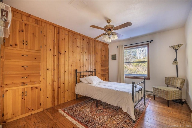 bedroom featuring ceiling fan, hardwood / wood-style flooring, baseboard heating, and wood walls