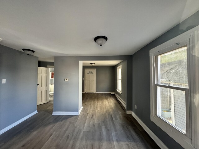 empty room with dark hardwood / wood-style flooring, a wealth of natural light, and baseboard heating