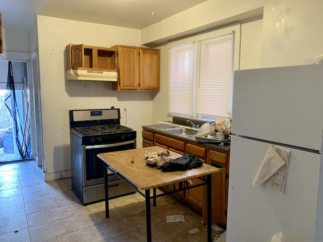 kitchen featuring sink, light tile patterned floors, stainless steel range with gas cooktop, and white fridge