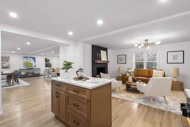 kitchen featuring light stone counters, a notable chandelier, a kitchen island, a brick fireplace, and light wood-type flooring