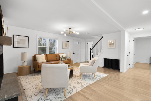 living room featuring a fireplace, light hardwood / wood-style floors, a notable chandelier, and radiator heating unit