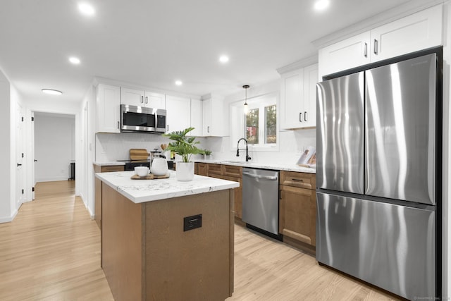 kitchen with hanging light fixtures, stainless steel appliances, light stone counters, white cabinets, and a center island