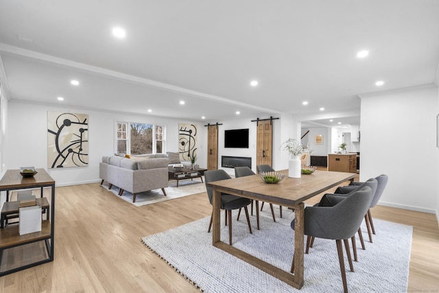 dining space with a barn door, crown molding, and light hardwood / wood-style flooring