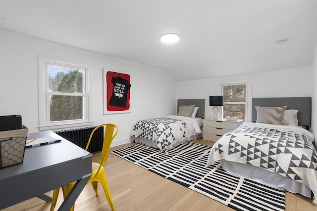 bedroom with hardwood / wood-style floors, multiple windows, vaulted ceiling, and radiator