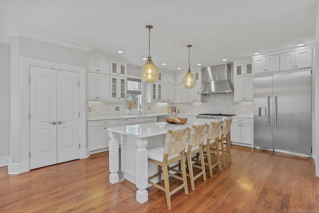 kitchen featuring stainless steel appliances, white cabinetry, a kitchen island, and wall chimney range hood