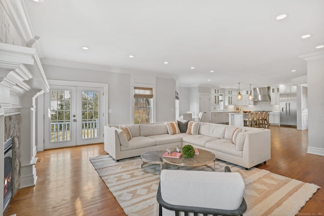 living room with french doors, crown molding, recessed lighting, light wood-type flooring, and a warm lit fireplace