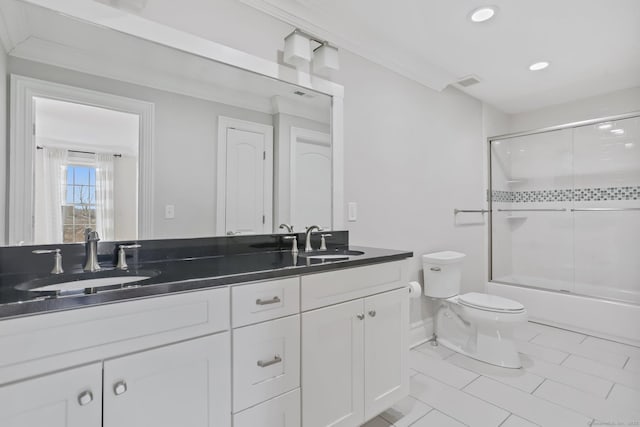 bathroom featuring double vanity, bath / shower combo with glass door, toilet, and a sink