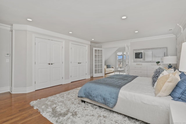 bedroom featuring two closets, recessed lighting, ornamental molding, wood finished floors, and baseboards