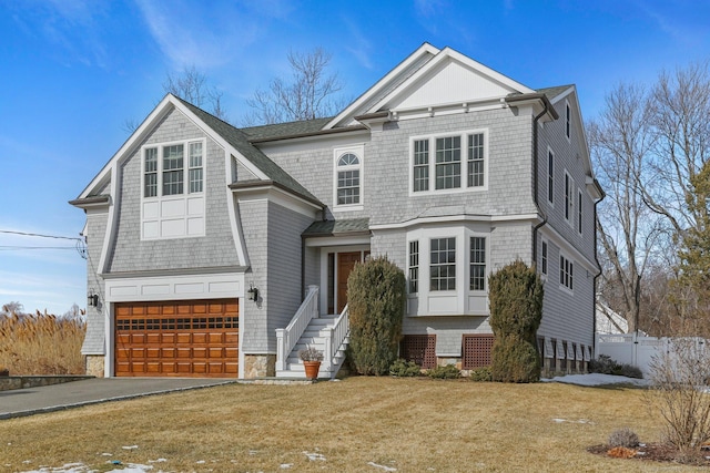 shingle-style home with a front yard, driveway, an attached garage, and fence