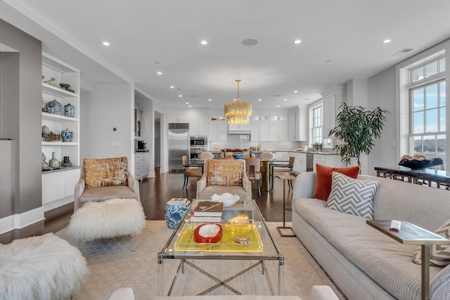 living room with an inviting chandelier, built in features, and light hardwood / wood-style floors