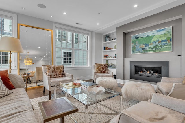 living room with built in shelves, a healthy amount of sunlight, and hardwood / wood-style flooring