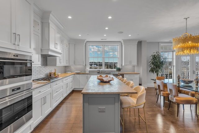 kitchen with stainless steel appliances, a kitchen breakfast bar, white cabinets, a kitchen island, and decorative light fixtures