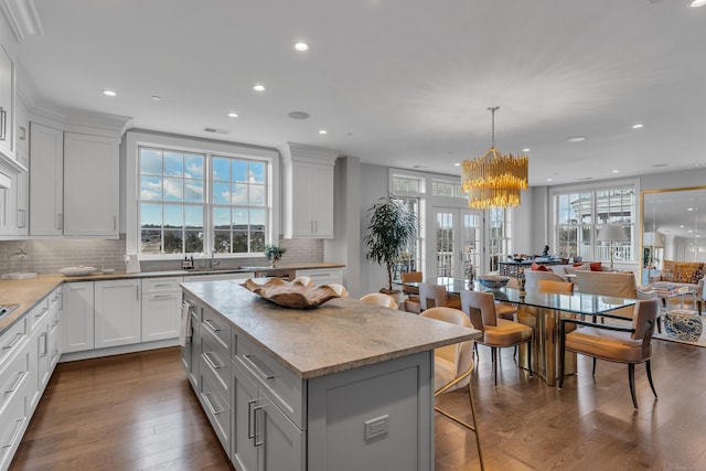 kitchen with decorative light fixtures, tasteful backsplash, white cabinetry, a center island, and dark wood-type flooring