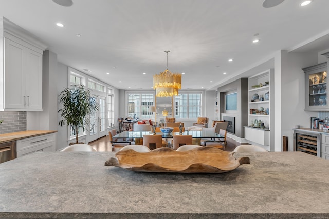 kitchen with a spacious island, white cabinetry, hanging light fixtures, beverage cooler, and decorative backsplash