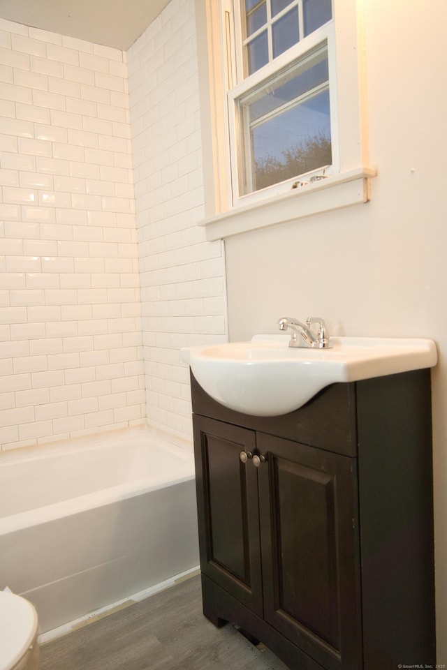 full bathroom with hardwood / wood-style flooring, tiled shower / bath, vanity, and toilet