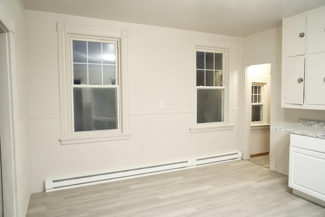 unfurnished dining area featuring a baseboard radiator and light wood-type flooring