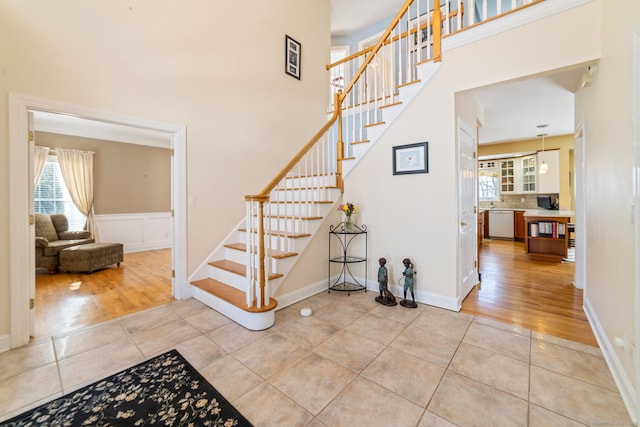 stairs with wainscoting, tile patterned flooring, and a towering ceiling