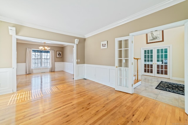 empty room with wainscoting, wood finished floors, an inviting chandelier, crown molding, and french doors