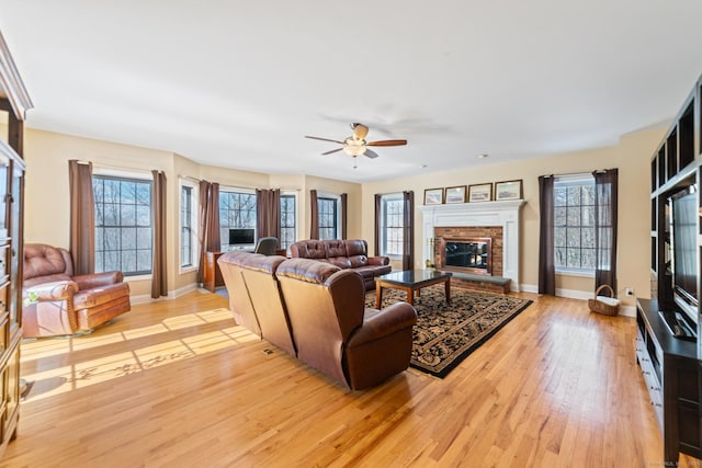 living room with light wood-type flooring, a fireplace, baseboards, and a ceiling fan