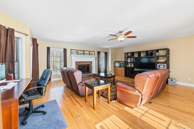 living room with light wood-style flooring, baseboards, ceiling fan, and a glass covered fireplace