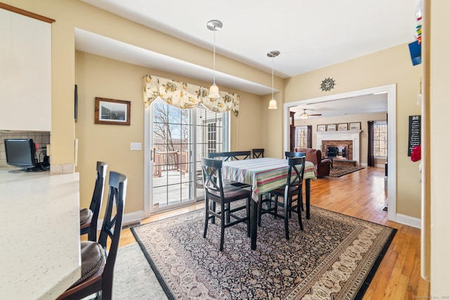 dining space featuring light wood-style floors, a brick fireplace, and baseboards