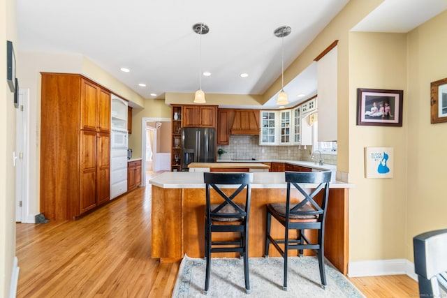 kitchen with light wood finished floors, stainless steel fridge with ice dispenser, a peninsula, light countertops, and premium range hood