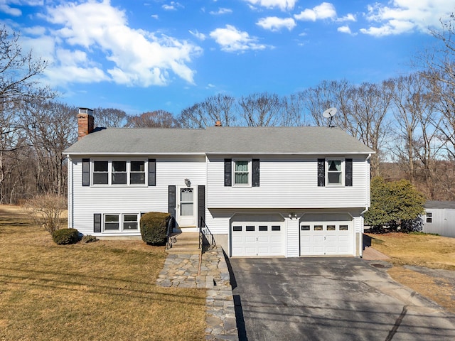 bi-level home featuring aphalt driveway, a chimney, a shingled roof, an attached garage, and a front yard