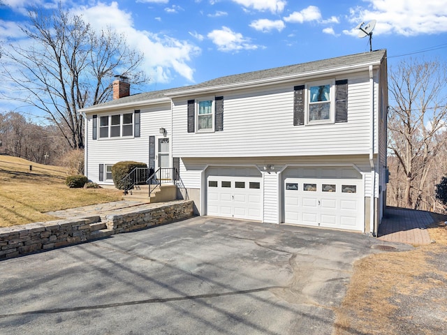 bi-level home with a garage, aphalt driveway, and a chimney