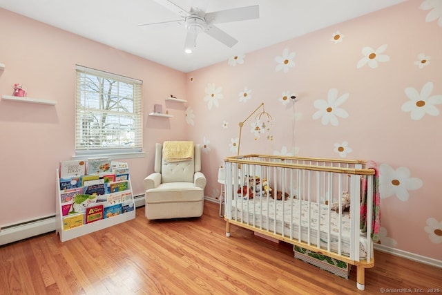 bedroom featuring a nursery area, hardwood / wood-style floors, and a baseboard heating unit